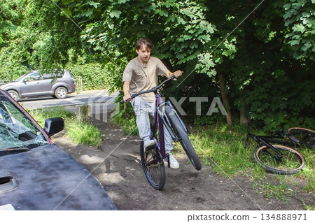 Teenage boy from Generation Z doing a bike trick on a narrow path near an abandoned car, surrounded by green trees. Urban youth lifestyle, freedom, adventure and street culture.  134888971