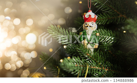 Traditional wooden nutcracker Christmas ornament hanging on a decorated Christmas tree with warm lights and golden baubles. Festive holiday atmosphere with cozy winter mood. Traditional wooden nutcracker Christmas ornament hanging on a decorated Christmas tree with warm lights and golden baubles. Festive holiday atmosphere with cozy winter mood. 134888986