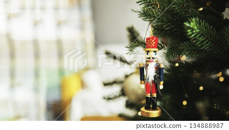 Traditional wooden nutcracker Christmas ornament hanging on a decorated Christmas tree with warm lights and golden baubles. Festive holiday atmosphere with cozy winter mood. 134888987