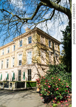 在倫敦郊區邱園，一棟淺棕色磚砌建築和咖啡館沐浴在湛藍的天空和明媚的陽光下。 134889055