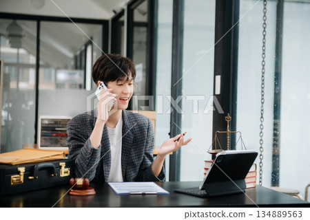 Asian female lawyer chatting online with client on laptop, smartphone  discussing details of lawsuit. in modern office 134889563