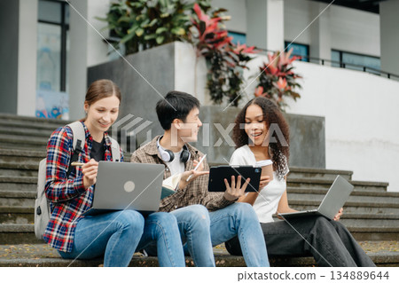 Two smart young Asian college students focusing on his school project, looking at laptop and tablet, discussing and working together Two smart young Asian college students focusing on his school project, looking at laptop and tablet, discussing and working together 134889644