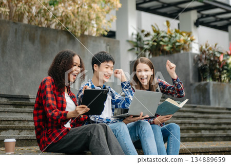 Two smart young Asian college students focusing on his school project, looking at laptop and tablet, discussing and working together 134889659