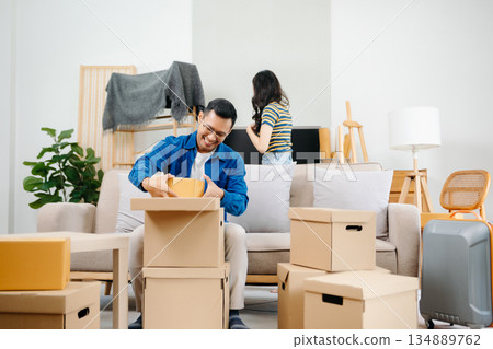 Young couple with big boxes moving into a new house, new apartment for couple, young man and woman helping to lift boxes on sofa for the new home, Moving house. Young couple with big boxes moving into a new house, new apartment for couple, young man and woman helping to lift boxes on sofa for the new home, Moving house. 134889762