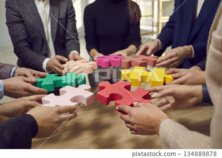Hands of a group of business people assembling jigsaw puzzle. Cooperation, teamwork support concept 134889878