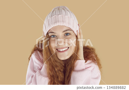 Close-up of face of beautiful smiling red-haired young woman wearing warm knitted pink hat. Close-up of face of beautiful smiling red-haired young woman wearing warm knitted pink hat. 134889882