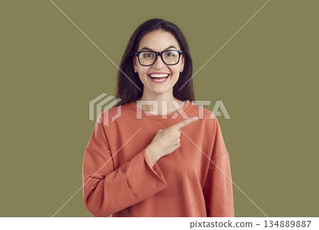 Woman with funny shocked face pointing finger to side showing offer or advertising deal. Woman with funny shocked face pointing finger to side showing offer or advertising deal. 134889887