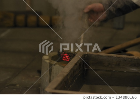 鐵匠將黏土汁液倒在燒紅的鐵塊上。 134890166