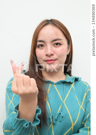 Portrait of a young Asian woman against white background making mini heart gesture 134890369