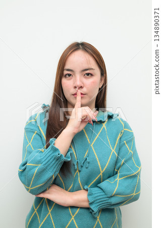 Portrait of a young Asian woman against white background with finger on lips Portrait of a young Asian woman against white background with finger on lips 134890371