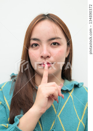 Portrait of a young Asian woman against white background with finger on lips 134890372