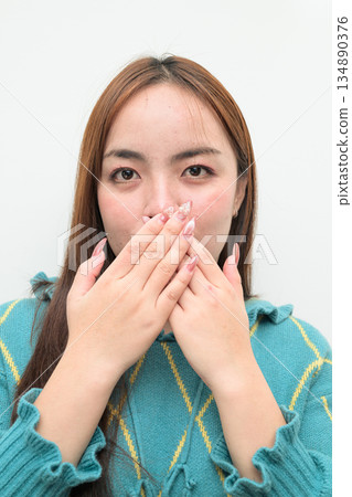 Portrait of a young Asian woman against white background covering mouth Portrait of a young Asian woman against white background covering mouth 134890376