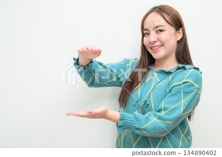Portrait of a young Asian woman against white background measuring amount with hands Portrait of a young Asian woman against white background measuring amount with hands 134890402