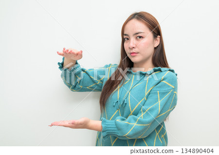 Portrait of a young Asian woman against white background measuring amount with hands Portrait of a young Asian woman against white background measuring amount with hands 134890404