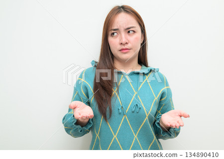 Portrait of a young Asian woman against white background shrugging shoulders with palms up Portrait of a young Asian woman against white background shrugging shoulders with palms up 134890410