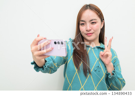 Portrait of a young Asian woman against white background using phone taking selfie Portrait of a young Asian woman against white background using phone taking selfie 134890433