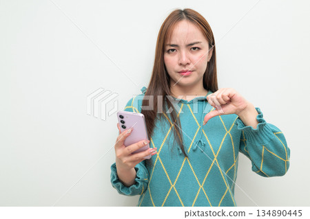 Portrait of a young Asian woman against white background using phone getting bad news Portrait of a young Asian woman against white background using phone getting bad news 134890445