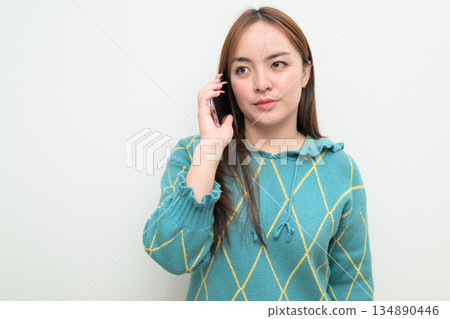 Portrait of a young Asian woman against white background on the phone talking Portrait of a young Asian woman against white background on the phone talking 134890446