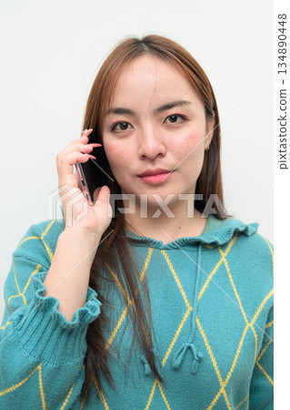 Portrait of a young Asian woman against white background on the phone talking Portrait of a young Asian woman against white background on the phone talking 134890448