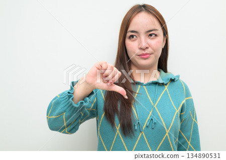 Portrait of a young Asian woman against white background with thumbs down gesture Portrait of a young Asian woman against white background with thumbs down gesture 134890531