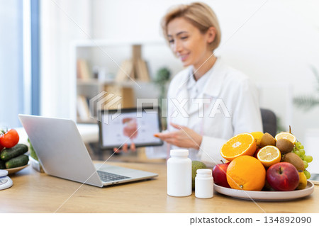 A nutritionist is giving an online consultation about healthy eating, with fruits and vegetables on the table. 134892090