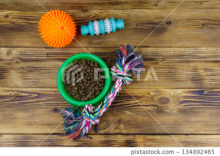 Dog toys and feed for dogs in green plastic bowl on wooden background. Top view. Dog care concept Dog toys and feed for dogs in green plastic bowl on wooden background. Top view. Dog care concept 134892465