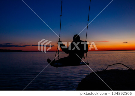 Silhouette of a man on rope swing above river at sunset Silhouette of a man on rope swing above river at sunset 134892506