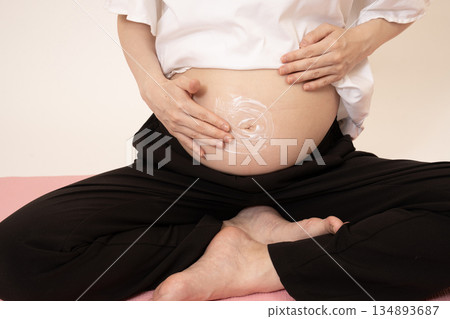 一名婦女在懷孕 8 個月的腹部塗抹乳霜 一名婦女在懷孕 8 個月的腹部塗抹乳霜 134893687
