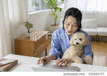 Middle-aged woman working on a computer and her pet dog. Image of working from home. 134893757