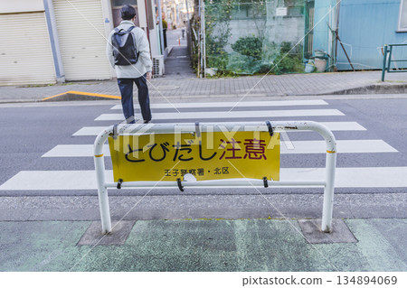 A sign warning of pedestrians jumping out and a crosswalk. A person walking in a residential area. 134894069
