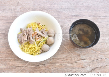 dry boiled Chinese yellow egg noodles with slice beef and meatball topping fried chop garlic on bowl with clear soup cup 134894105