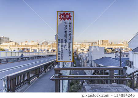 A pedestrian bridge with a warning sign encouraging cyclists to slow down. A view of a residential area and an elevated road. A pedestrian bridge with a warning sign encouraging cyclists to slow down. A view of a residential area and an elevated road. 134894246