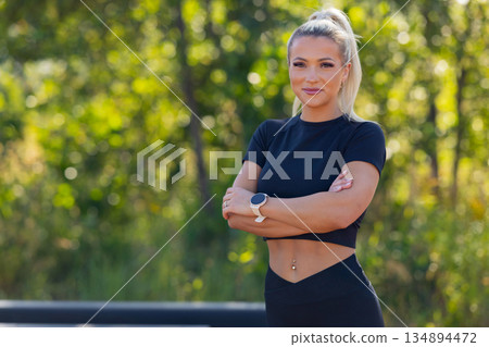 Confident woman in fitness attire outdoors with smartwatch 134894472