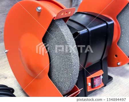 Close-up of an orange bench grinder in a workshop setting. 134894497