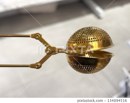Gold metal tea infuser with a perforated design. 134894516
