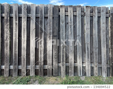 A rustic wooden fence with vertical planks. 134894522
