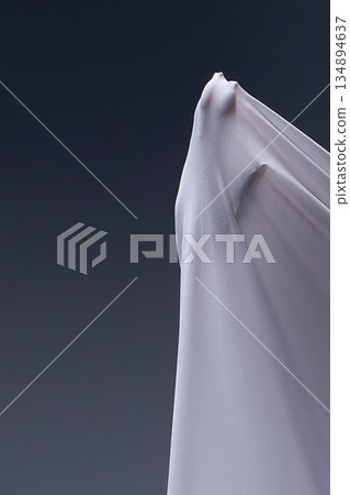A human hand presses against taut white fabric, creating an abstract, sculptural form against a dark gray background. 134894637