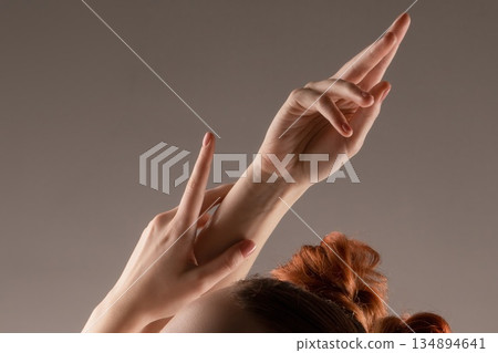 Elegant female hands and arms raised in a graceful, artistic pose against a neutral background Elegant female hands and arms raised in a graceful, artistic pose against a neutral background 134894641