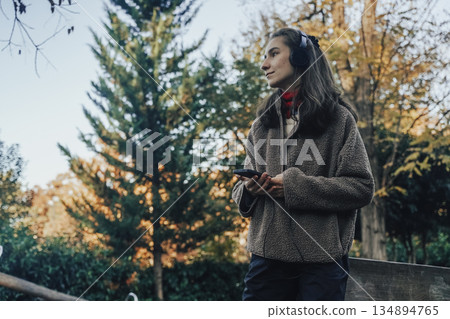Peaceful Woman Relaxing and Listening to Music in Autumn Park Peaceful Woman Relaxing and Listening to Music in Autumn Park 134894765