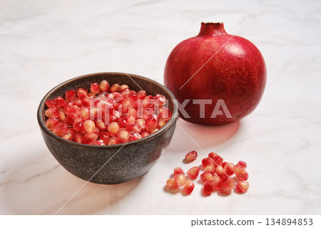 Pomegranate fruit and seeds in a bowl on a light countertop Pomegranate fruit and seeds in a bowl on a light countertop 134894853