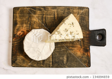 Cheese placed on a wooden board with one wedge cut and another whole piece beside it Cheese placed on a wooden board with one wedge cut and another whole piece beside it 134894859