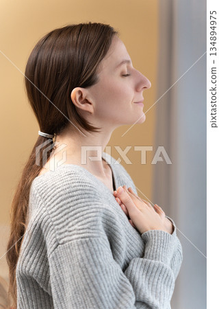 Portrait serene peaceful young Caucasian woman with closed eyes practicing deep breathing, hands on chest, feeling calm and peaceful, demonstrating stress relief, inner peace and mindfulness concept Portrait serene peaceful young Caucasian woman with closed eyes practicing deep breathing, hands on chest, feeling calm and peaceful, demonstrating stress relief, inner peace and mindfulness concept 134894975