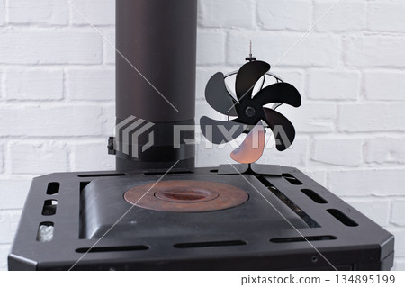 Stove fan heat powered. Black heat stove fan on the top of wood stove to improve heat circulation. Eco-friendly home heating concept Stove fan heat powered. Black heat stove fan on the top of wood stove to improve heat circulation. Eco-friendly home heating concept 134895199
