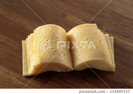 Cheese slices folded like an open book on a wooden table. 134895537
