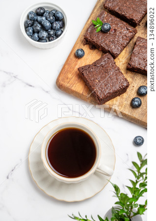 Pieces of chocolate brownie on a wooden board and a cup of espresso coffee on a light background Pieces of chocolate brownie on a wooden board and a cup of espresso coffee on a light background 134896022