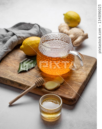 Hot ginger lemon tea in glass cup on wooden board with honey and fresh ingredients. Hot ginger lemon tea in glass cup on wooden board with honey and fresh ingredients. 134896025