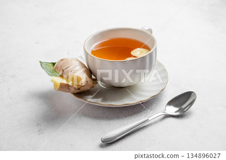 A cup of hot tea with ginger on a light textured background with fresh root and spoon. 134896027