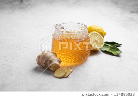 A glass cup of hot tea with fresh lemon and ginger on a light textured background 134896028