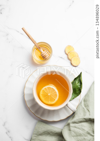 A cup of hot tea with fresh lemon and ginger on a light marble background with honey 134896029