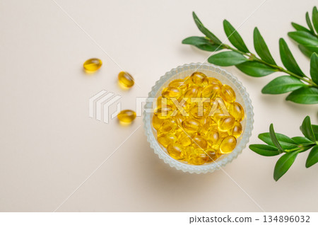 Yellow softgel vitamins capsules in a bowl on a light background with green leaf. Yellow softgel vitamins capsules in a bowl on a light background with green leaf. 134896032